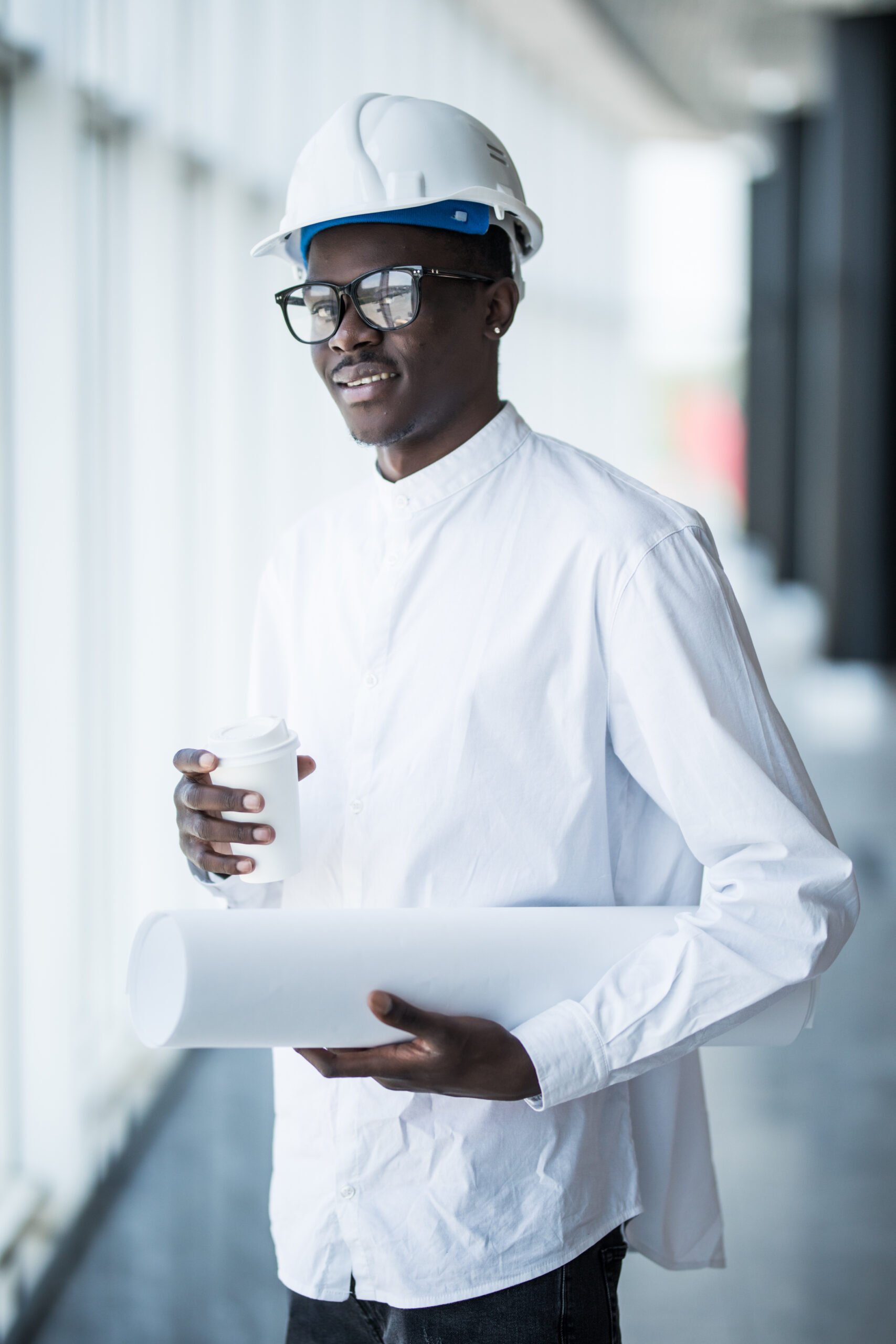 Young Afro-American engineer with blue prints in front of panoramic windows in office